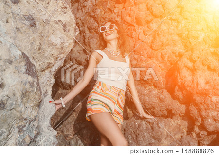 Woman rocky cliff stands in bright sunlight while wearing summer clothing on a tropical beach adventure Woman rocky cliff stands in bright sunlight while wearing summer clothing on a tropical beach adventure 138888876