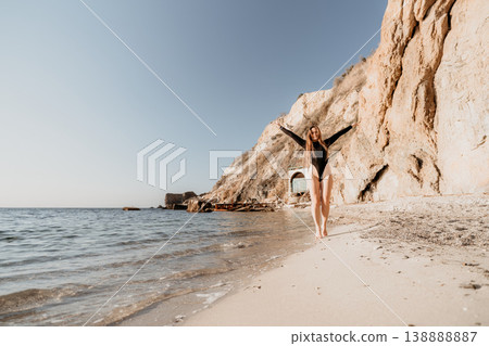 Woman beach vacation happy woman in black swimsuit walks on a sandy beach with arms open wide by the ocean cliffs 138888887