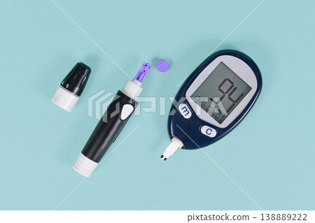 Tools for diabetes treatment with blood glucose sugar meter showing blood sugar of 94 and lancing device with lancet on blue background 138889222