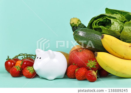 Concept for costs of healthy eating or saving money when buying food. Vegetables and fruits next to piggy bank on blue background with copy space Concept for costs of healthy eating or saving money when buying food. Vegetables and fruits next to piggy bank on blue background with copy space 138889245