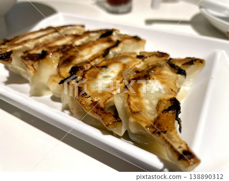 Pan-fried dumplings - served on a long white plate with a nicely browned surface. Pan-fried dumplings - served on a long white plate with a nicely browned surface. 138890312