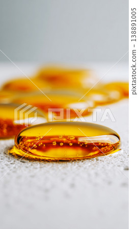 Small yellow oil drops rest on a flat surface, reflecting light. The close-up shows details of each drop, highlighting their size, shape, and surrounding surface Small yellow oil drops rest on a flat surface, reflecting light. The close-up shows details of each drop, highlighting their size, shape, and surrounding surface 138891005