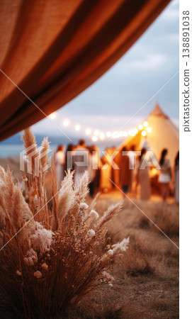 Guests gather under a large wedding tent filled with warm lights. The area is decorated with flowers and creates a festive ambiance for the outdoor celebration at dusk Guests gather under a large wedding tent filled with warm lights. The area is decorated with flowers and creates a festive ambiance for the outdoor celebration at dusk 138891038