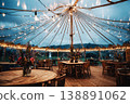 Guests are seated at wooden tables inside a wedding tent. Strings of lights hang from the top. The view shows water and city lights in the background during the evening 138891062