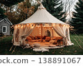 A wedding tent is set up in a grassy space with trees around. Inside, there are cushions and lights creating a cozy atmosphere for guests to relax and enjoy 138891067