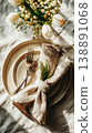 The table is set for a wedding with plates, folded linen napkins, and greenery as accents. Glasses of water sit next to each place setting in a bright indoor setting 138891068