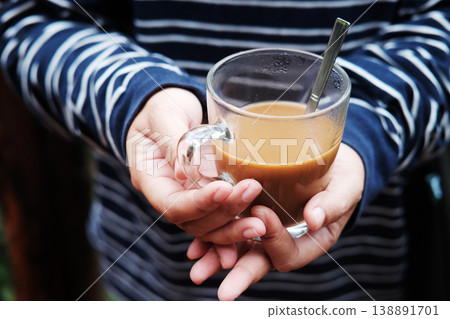 Close up Silhouette of hand holding a glass cup of hot coffee in natural green forest background Close up Silhouette of hand holding a glass cup of hot coffee in natural green forest background 138891701
