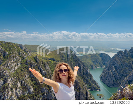 Hiker woman on the background of a mountain river. Girl traveler stands on the edge of rock 138892003