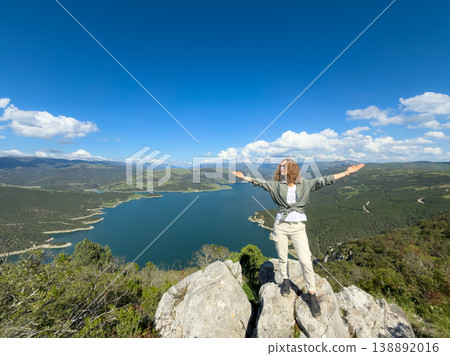 Hiker woman on the background of a mountain river. Girl traveler stands on the edge of rock Hiker woman on the background of a mountain river. Girl traveler stands on the edge of rock 138892016