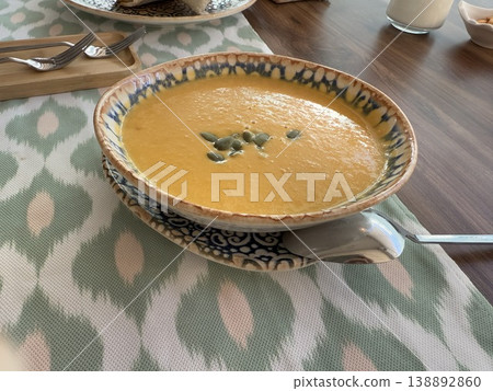 Pumpkin soup in patterned bowl topped with pumpkin seeds on wooden table background 138892860
