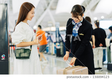 A female airport ground staff member attaches a tag to a traveler's carry-on bag. (Photo courtesy of Kansai International Airport (KIX)) A female airport ground staff member attaches a tag to a traveler's carry-on bag. (Photo courtesy of Kansai International Airport (KIX)) 138894123