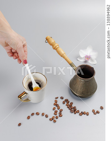 Woman's hand with a cup of coffee. Cezve with roasted coffee beans and an orchid flower. 138894962