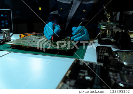 Computer Hardware Technician Repairing Motherboard with Soldering Iron in Electronics Lab. 138895302