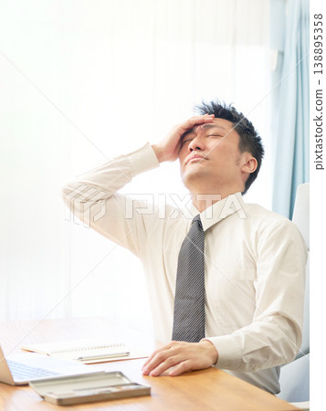 A businessman holding his head and looking exhausted during work. 138895358