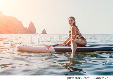 Woman Paddleboard Ocean - Woman sitting on a paddleboard in the ocean, enjoying the water and sunshine. Woman Paddleboard Ocean - Woman sitting on a paddleboard in the ocean, enjoying the water and sunshine. 138895732