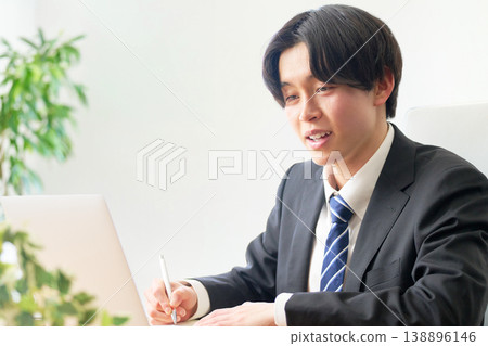 A highly motivated businessman smiles and writes with a pen while looking at his computer screen. A highly motivated businessman smiles and writes with a pen while looking at his computer screen. 138896146