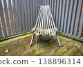 Folded wooden deck chair on weathered terrace with gray fence and rustic outdoor texture 138896314
