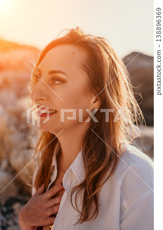 Woman beach sunset smiling middle aged female in white shirt enjoys golden hour at rocky coastline with warm light Woman beach sunset smiling middle aged female in white shirt enjoys golden hour at rocky coastline with warm light 138896369
