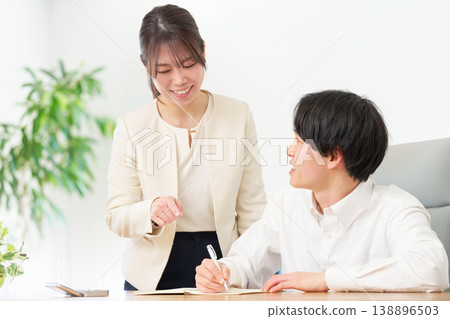 A young man takes notes while being taught by a woman in a suit. A young man takes notes while being taught by a woman in a suit. 138896503
