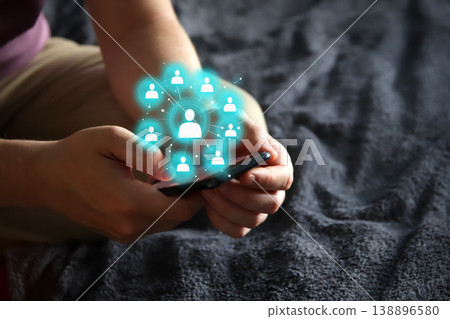 Close-up of male hands holding a smartphone with a glowing digital social network icon overlay. Concept of global communication, networking, human resources, and digital connectivity Close-up of male hands holding a smartphone with a glowing digital social network icon overlay. Concept of global communication, networking, human resources, and digital connectivity 138896580