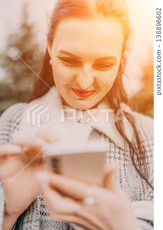 Woman smartphone sunset smiling while using mobile phone outdoors in golden hour light with warm lens flare Woman smartphone sunset smiling while using mobile phone outdoors in golden hour light with warm lens flare 138896602