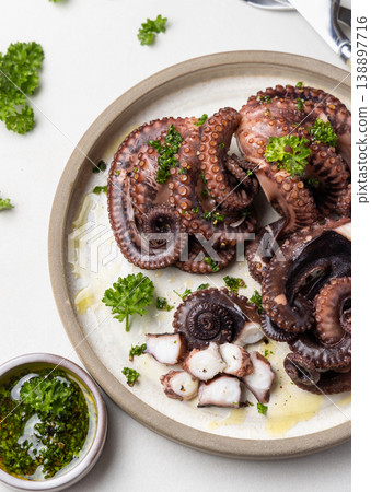 Boiled octopus tentacles and sliced pieces on ceramic plate top view. Olive oil and parsley dressing Boiled octopus tentacles and sliced pieces on ceramic plate top view. Olive oil and parsley dressing 138897716