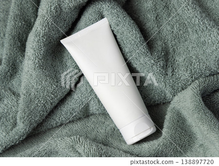 White blank cream tube on sage green bath towel top view, cosmetic packaging mockup 138897720