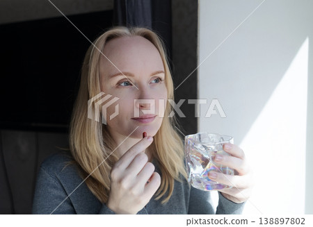 Woman taking iron supplement capsule with glass of water. Female health care, iron deficiency anemia treatment, vitamins and minerals intake for wellness. Woman taking iron supplement capsule with glass of water. Female health care, iron deficiency anemia treatment, vitamins and minerals intake for wellness. 138897802