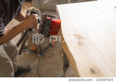 Woodworker sanding natural live edge wood slab in workshop 138897835