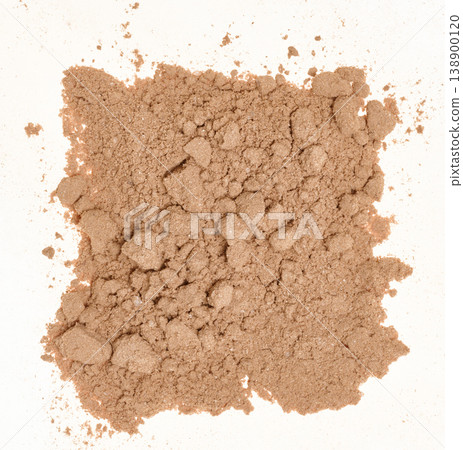 Spilled cocoa powder with small lumps, forming an uneven textured spot on a white background. Spilled cocoa powder with small lumps, forming an uneven textured spot on a white background. 138900120