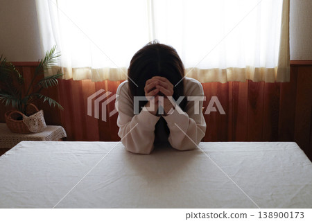 A woman, with her hair unkempt and still in her loungewear, hangs her head listlessly. A woman, with her hair unkempt and still in her loungewear, hangs her head listlessly. 138900173