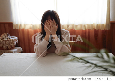 A woman, still in her loungewear and with her hair unkempt, weakly covers her face. A woman, still in her loungewear and with her hair unkempt, weakly covers her face. 138900180