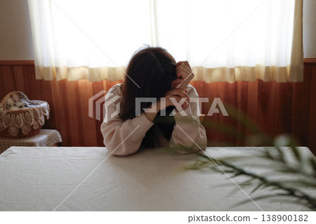 A woman, with her hair unkempt and still in her loungewear, hangs her head listlessly. 138900182