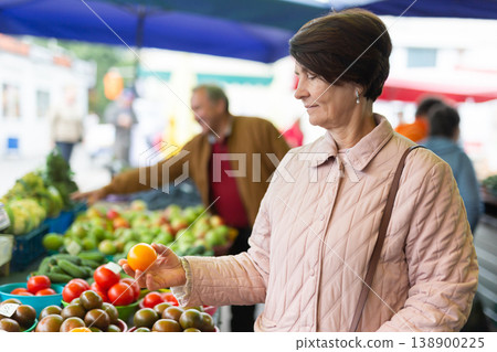 elderly woman buys vegetables at an open market elderly woman buys vegetables at an open market 138900225