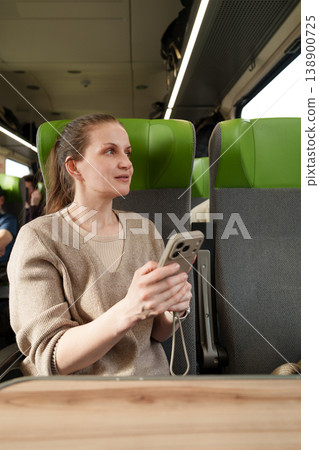 Brunette Caucasian woman using smartphone while traveling by train. Brunette Caucasian woman using smartphone while traveling by train. 138900725
