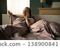 Young woman relaxing in her bedroom, smiling and laughing while having a casual phone call on her smartphone in bed, enjoying morning communication and connection 138900841