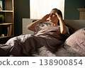 Woman waking up in the morning, suffering from a painful migraine and headache, holding temples with hands while lying in bed, feeling unwell and tired from stress and lack of sleep 138900854