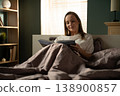 Young woman happily reading a book in bed during leisure time, enjoying a peaceful hobby and quiet evening routine in the comfort of her modern bedroom 138900857