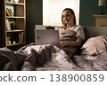 Woman comfortably relaxing in bed, browsing online her laptop, enjoying a relaxed morning at home while staying connected with technology and daily tasks 138900859