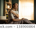 Woman sitting in bed, holding her shoulder in discomfort, feeling an injury or muscle ache after waking up, highlighting concepts of pain, exhaustion, and healthcare 138900864