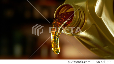 Close-up of motor oil pouring from a plastic container. Golden viscous liquid with bubbles flowing smoothly, automotive maintenance concept with shallow depth of field. Close-up of motor oil pouring from a plastic container. Golden viscous liquid with bubbles flowing smoothly, automotive maintenance concept with shallow depth of field. 138901088