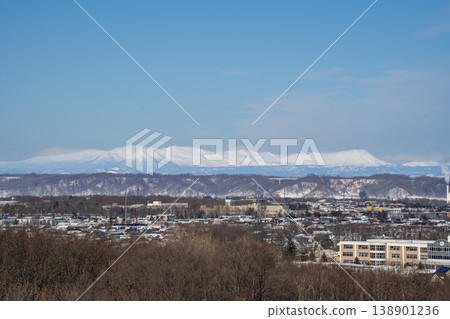 冬日的北海道：城鎮風光，遠方是白雪皚皚的山脈。這壯麗的景色展現了北海道的自然風光。皚皚雪峰在湛藍的天空映襯下，閃耀著冬日的光芒。 138901236