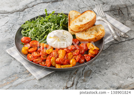 Delicious Italian burrata, baked cherry tomatoes and fresh arugula with olive oil and toasted ciabatta close-up in a plate. Horizontal 138901824
