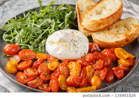 Starter of burrata, roasted cherry tomatoes and fresh arugula with olive oil and toasted ciabatta close-up in a plate. Horizontal 138901826