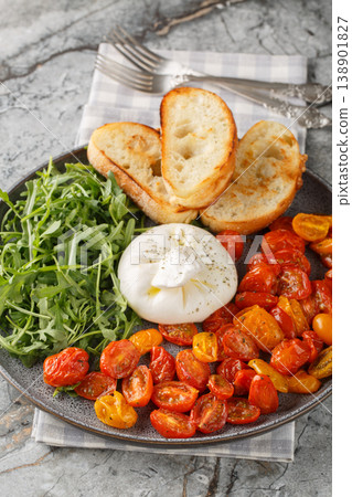 Appetizer of burrata, baked cherry tomatoes and fresh arugula close-up in a plate. Vertical 138901827