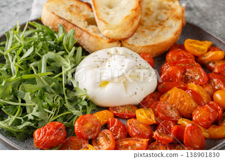 burrata salad with roasted cherry tomatoes, fresh arugula, olive oil, and toasted ciabatta on a plate. Horizontal burrata salad with roasted cherry tomatoes, fresh arugula, olive oil, and toasted ciabatta on a plate. Horizontal 138901830