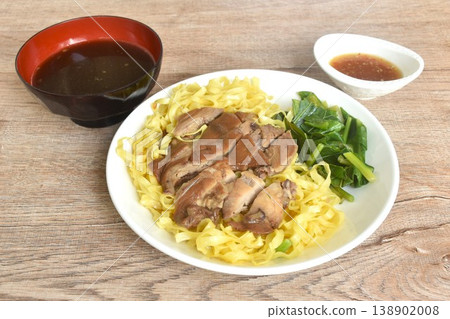 Chinese yellow egg nodles topping braised slice pork leg stew dressing black herb soup couple pickled cabbage and kale dipping spicy sour chili sauce on plate 138902008