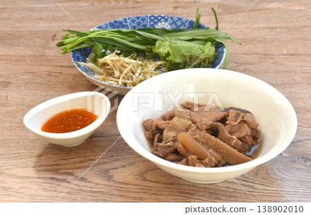 boiled braised beef meat and tendon couple organ in herb brown soup on bowl with fresh vegetable dipping spicy chili sauce 138902010