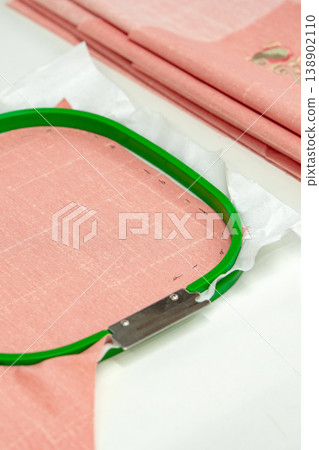 Crafting with fabric using an embroidery hoop on a workspace with pink cloth 138902110