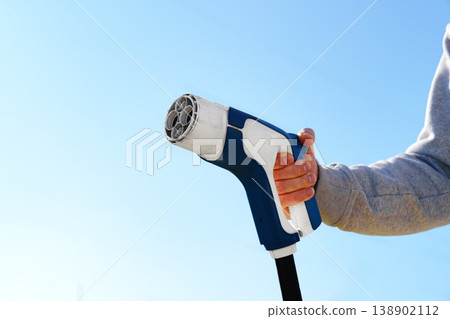 Electric car charger held by a person against a clear blue sky during daylight 138902112